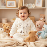 A baby girl wearing a hooded jacket with a teddy bear design and a pair of matching pants.