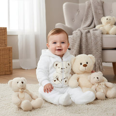A baby girl wearing a white hooded jacket with a teddy bear design and the matching white pants.