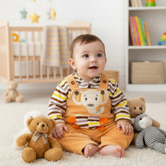 A baby in a brown velvet dungaree dress with a hooded shirt featuring a bear face design in a striped pattern.