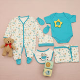 A set of baby boy clothing and accessories including a bodysuit, romper, bib, cap, and mittens, laid out on a wooden surface. The clothing is primarily blue with a pattern of sea creatures and plants.