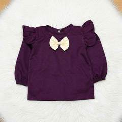 Purple children's top with a yellow bow on a white surface with flowers.