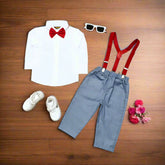 Children's outfit with white shirt, red bow tie, gray pants, red suspenders, and white shoes on a wooden surface.