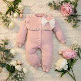 Pink baby romper with a white bow on a wooden surface
