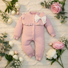 Pink baby romper with a white bow on a wooden surface