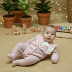 Pink baby romper with a white bow on a wooden surface