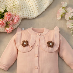 Pink knitted cardigan with brown flower decorations on a wooden surface