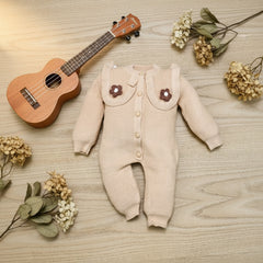 Beige baby romper with flower details on a wooden surface