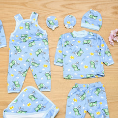 Baby clothing set with blue overalls, shirt, pants, and hat featuring green dinosaur prints on a wooden surface.