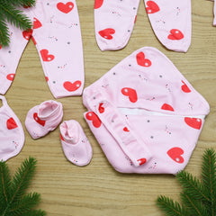 Baby clothing set with pink and red heart patterns on a wooden surface