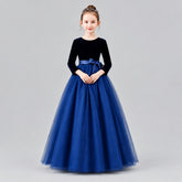A young girl modeling a formal ball gown with a velvet long-sleeve bodice, a silk waistband, and a voluminous tulle skirt.