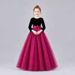 A young girl modeling a formal ball gown with a velvet long-sleeve bodice, a satin waistband, and a voluminous tulle skirt, set against a solid beige studio background.
