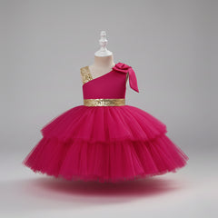 A pink one-shoulder toddler party dress with a tiered tulle skirt, a gold sequined waistband, and a matching bow on the shoulder.