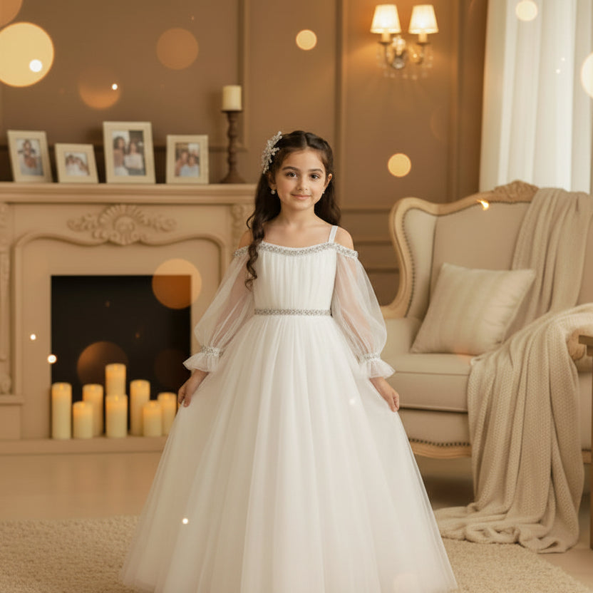 A young girl wearing a white off-the-shoulder tulle ball gown with silver beaded trim at the neckline and waist.
