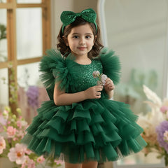 Young girl in a bottle green dress with ruffles standing in a decorated room with flowers.