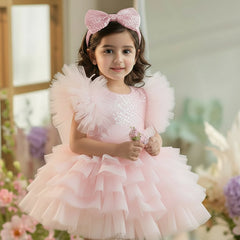 Young girl in a pink dress with ruffles standing in a decorated room with flowers.