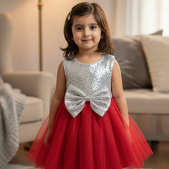 Young girl in a red and silver dress with a bow standing in a living room.