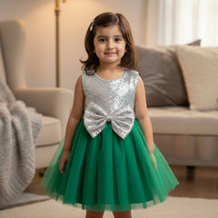 Young girl in a green and silver dress with a bow standing in a living room.