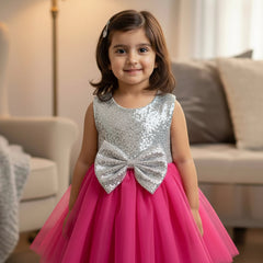 Young girl in a hot pink and silver dress with a bow standing in a living room.