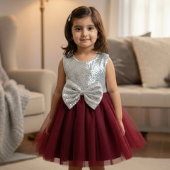 Young girl in a maroon and silver dress with a bow standing in a living room.
