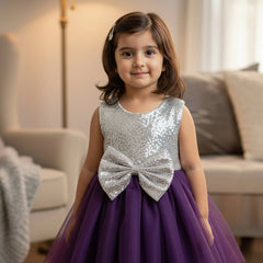 Young girl in a purple and silver dress with a bow standing in a living room.