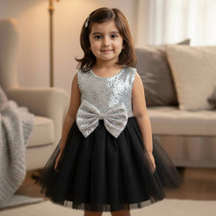 Young girl in a black and silver dress with a bow standing in a living room.