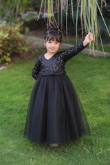 A young girl wearing a long-sleeve ball gown with sequined detailing and a matching headpiece, standing on a green lawn outdoors.