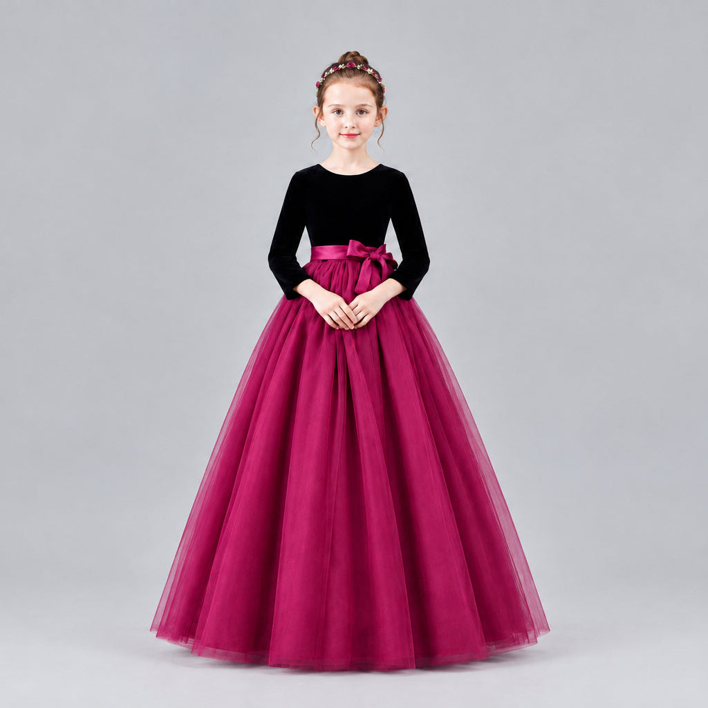 A young girl modeling a formal ball gown with a velvet long-sleeve bodice, a satin waistband, and a voluminous tulle skirt, set against a solid beige studio background.