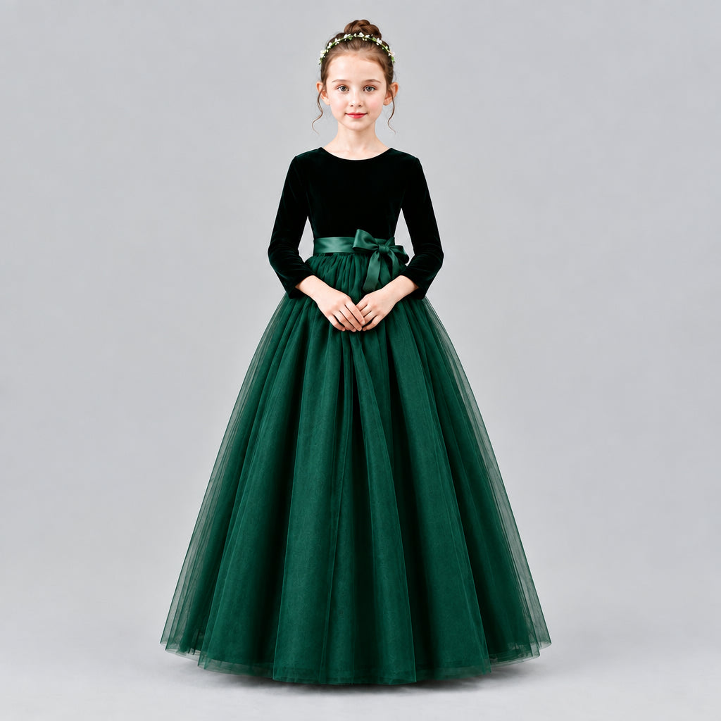 A young girl modeling a formal ball gown with a velvet long-sleeve bodice, a satin waistband, and a voluminous tulle skirt, set against a solid beige studio background.