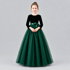 A young girl modeling a formal ball gown with a velvet long-sleeve bodice, a satin waistband, and a voluminous tulle skirt, set against a solid beige studio background.