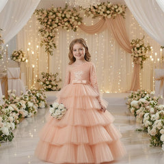 A young girl stands in a decorated event space wearing a formal one-shoulder ball gown with a sparkling upper bodice, a wide silk waistband, and a full layered tulle skirt. 