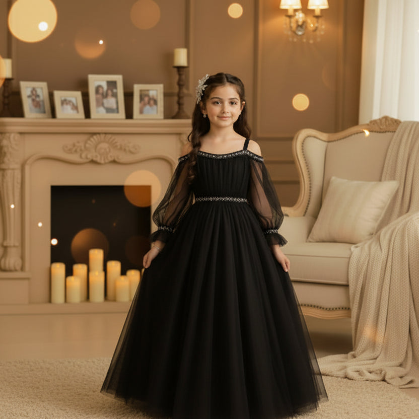 A young girl wearing a black off-the-shoulder tulle ball gown with silver beaded trim at the neckline and waist.