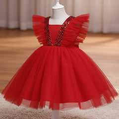 A red children's party dress displayed on a white dress form mannequin. The dress features a voluminous tulle skirt, ruffled cap sleeves, and a V-neckline embellished with sparkling silver sequins, set against a warm indoor background with a wooden floor and beige curtains.