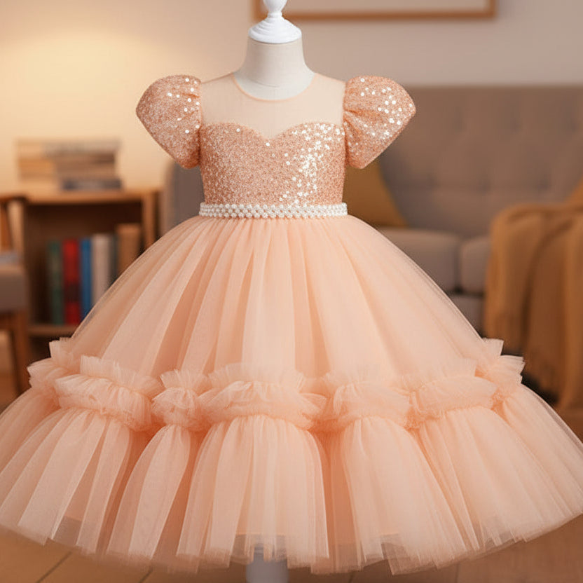 A turquoise blue sequined girl's party dress with puff sleeves and a tiered tulle skirt, displayed on a white mannequin in a cozy living room setting.