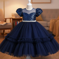 A navy girls' party dress displayed on a mannequin. The dress features a beaded off-the-shoulder bodice with puff sleeves, a pearl-embellished waistband, and a voluminous tiered tulle skirt.